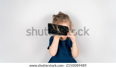 Portrait of terrified child with damaged phone. Upset little girl breaks screen of mobile phone. Kid girl holding broken display. Worried child accidentally destroyed smartphone