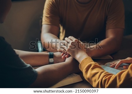 Christian family sitting around a wooden table with open bible page and holding hands to bless and pray for each other. comforting and praying together.Christians and Bible study concept.

  Royalty-Free Stock Photo #2150090397