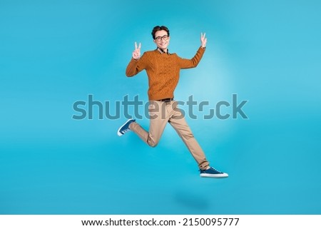 Full size photo of young man jump show fingers peace cool v-symbol isolated over blue color background