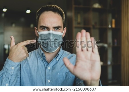 Mandatory wearing of a mask in a public place. Warning. The evil guard forbids passing without a mask. The man shows a stop gesture with his hand. do not enter. mask mode