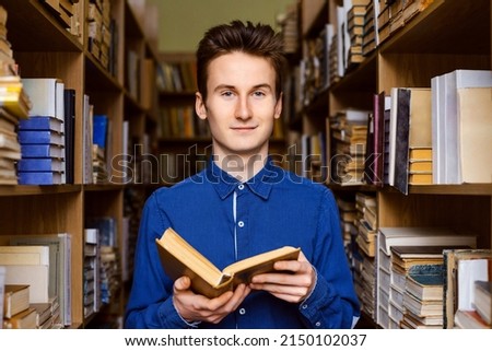 Male student finding information in books, preparing for exams. Portrait of young student in the library with a book in his hands