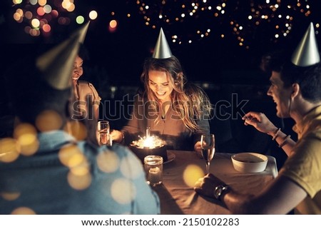 Shes celebrating her birthday with all her close friends. Shot of a group of friends celebrating a birthday together around a table at a gathering outdoors in the evening.