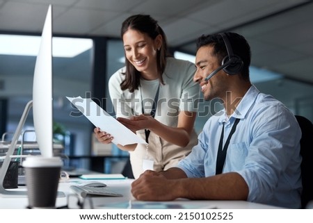 Collaboration gets those queues cleared. Shot of a young man and woman reading a document while working in a call centre. Royalty-Free Stock Photo #2150102525