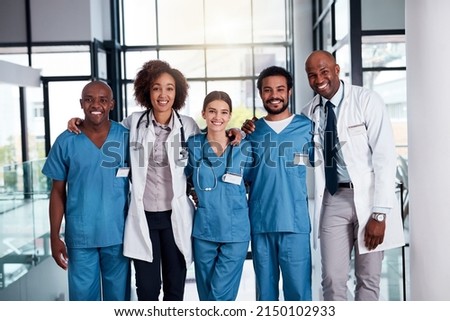 They will take care of your medical needs. Portrait of a cheerful group of doctors standing with their arms around each other inside of a hospital during the day. Royalty-Free Stock Photo #2150102933