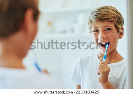 Keeping my teeth strong. Shot of a cheerful young boy looking at his reflection in a mirror while brushing his teeth in the bathroom at home during the day. Royalty-Free Stock Photo #2150103425