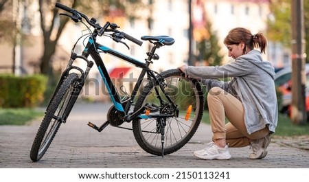 Young girl checking pressure of bike's tyres in the autumn park.