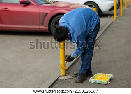 Painting a metal post with yellow paint. Parking bollard painting. Paints with a roller with yellow paint.