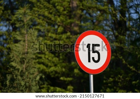 Traffic sign indicator showing the maximum speed limit at 15 kmh photographed against forest background. Slow speed announcement. Transportation industry.