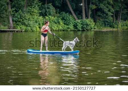Woman standing on paddle sup board with her white dog.