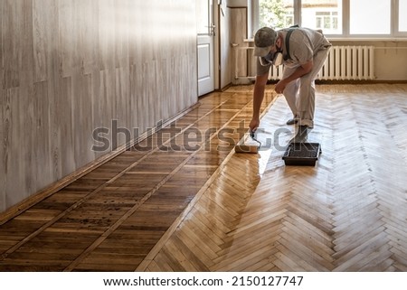 Profesional worker lacquering parquet floors using roller Royalty-Free Stock Photo #2150127747