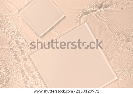 Two empty clear glass square podiums on beige transparent calm water texture with waves in sunlight. Abstract nature background for product presentation. Flat lay cosmetic mockup, copy space.