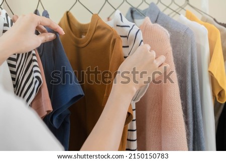 Choice of clothes, Nothing to wear asian young woman, girl hand in choosing dress, outfit on hanger in wardrobe in room closet at home. Deciding what to put on which one. Royalty-Free Stock Photo #2150150783