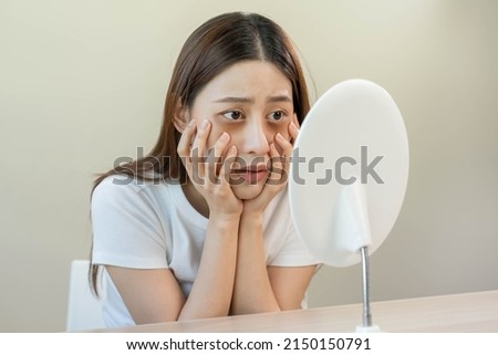 Bored, insomnia asian young woman, girl looking at mirror, without makeup, touch under eyes with problem of dark circles, puffiness, swollen or wrinkles on face. Sleepless, sleepy people, copy space Royalty-Free Stock Photo #2150150791