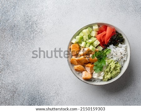 Salmon poke (buddha bowl) with avocado puree, cucumber cubes, pickled ginger, dry nori seaweed, cream cheese, sesame seeds and rice. Healthy seafood dish, lunch or dinner. Top view. Copy space.