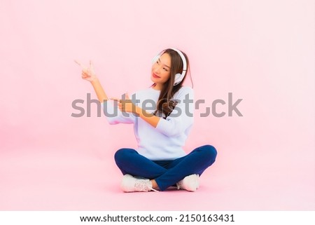 Portrait beautiful young asian woman use smart mobile phone with headphone for listen music on pink background