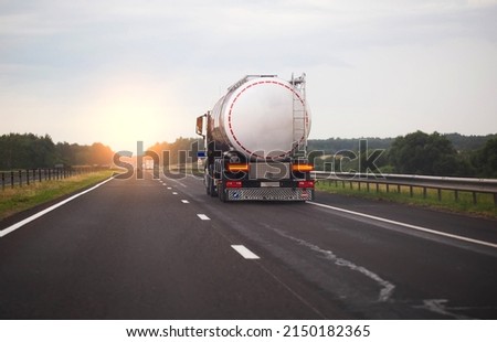 A truck with a semi-trailer transports a dangerous chemical cargo in a tank car on a highway against the background of a sunset. Sanctions in cargo transportation, capacity Royalty-Free Stock Photo #2150182365