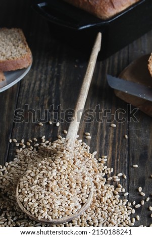 Wooden spoon filled with hard white wheat berries with a freshly baked loaf of bread in pan. Selective focus with blurred background.
