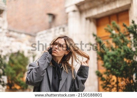 Upset woman. Woman talking sad by the bad news she hear on the cell mobile phone. Gloomy girl short hair wear grey suit and twisting a lock of hair on her finger. Royalty-Free Stock Photo #2150188801