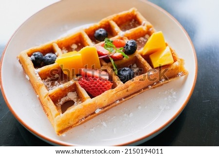 Waffle with Fresh Fruits. Waffles with berries and icing sugar on a white plate. Waffles with strawberries, blueberries, mango and sugar, homemade breakfast.