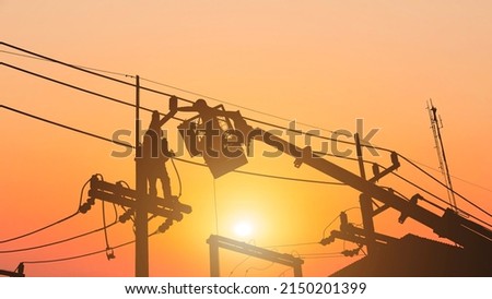 Silhouette workers installing electrical equipment on utility poles.