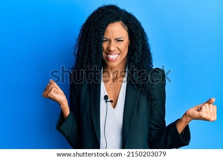 Middle age african american woman using lavalier microphone screaming proud, celebrating victory and success very excited with raised arm 