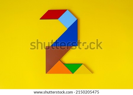 Colorful number 2 made with tangram toy, colored tangram number two isolated on yellow background, kids game idea, teaching counting for children, puzzle toy, top view of second numeric