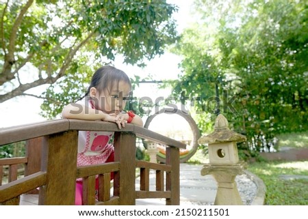 Lonely kid girl sitting alone at garden. Child thinking about something.              