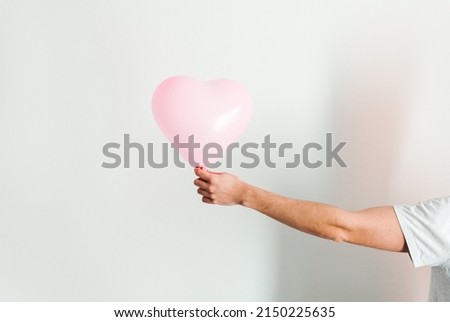 Pink inflatable heart-shaped balloon in hand. White background.