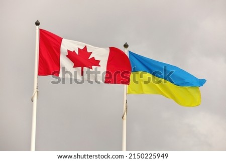 Canada and Ukraine national flags waving in wind against cloudy sky. Ukrainian and Canadian Flag