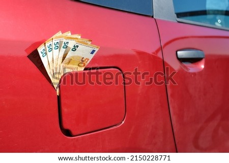 Fifty euro notes sticking out of a car's closed fuel tank, raising fuel price  Royalty-Free Stock Photo #2150228771