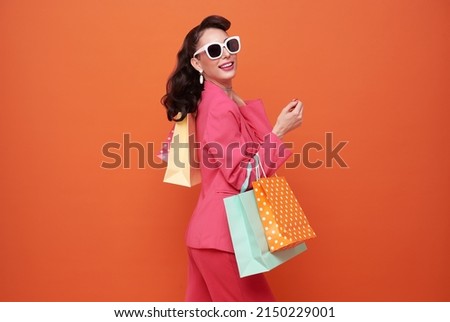 Cheerful happy woman enjoying shopping, she is carrying shopping bags on orange background.