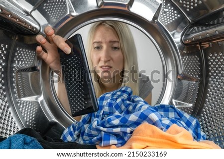 Disappointed young blonde woman finds her mobile phone in the washing machine after washing clothes, photo from inside