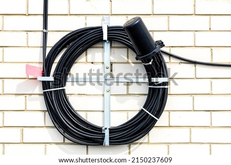 an optical coupling hangs on the wall, an optical cable is brought into it from different sides. supply of optical cable assembly in a black sleeve Royalty-Free Stock Photo #2150237609