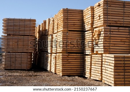 Rough pine lumber stacked at the sawmill. Woodworking plant and sawn timber in stacks for shipment for export. Wooden boards, lumber, commercial timber. Pine timber. Royalty-Free Stock Photo #2150237667