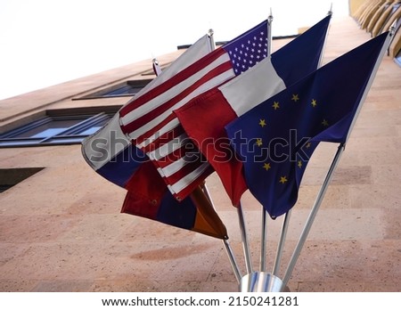 Many different flags hanging from the building. European union, France, United States of America, Armenia and Russian Federation. 