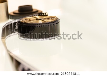 Rolls of film with a section of unrolled film showing individual frames on a  light table with equipment in the background. With space for free text. Selective focus.
