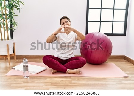 Young hispanic woman training at sport center smiling in love doing heart symbol shape with hands. romantic concept. 