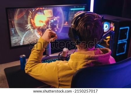 Back view of streamer young man rejoices his victory in esport shooter game tournament, making winner hand gesture. Professional gamer streaming online gameplay competition. Cyber sport concept Royalty-Free Stock Photo #2150257017