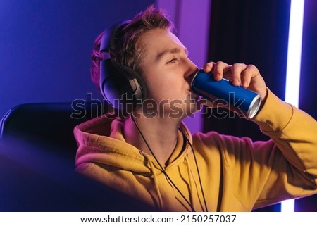 Young professional cybersport gamer playing online video game late at night, drinking caffeine energy drink to wake up and concentrate, focus on multiplay tournament. Games addiction concept Royalty-Free Stock Photo #2150257037