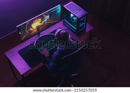 Top view of professional cyber sportsman in headphones playing shooter video game on his powerful gaming PC in dark neon room at night. Pro gamer participates in online esport tournament. Cyber sport Royalty-Free Stock Photo #2150257059