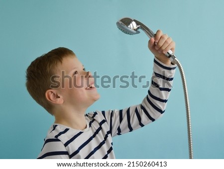 A happy smiling boy with a watering can from the shower over his head on a blue background. The concept of housewarming, renovation, happy childhood. Place fo text. Royalty-Free Stock Photo #2150260413