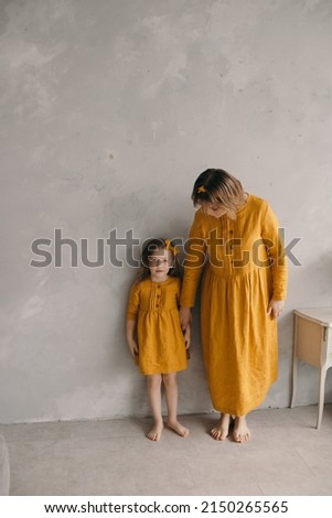 mom and daughter in yellow beautiful dresses are standing near the textured wall hugging, having fun