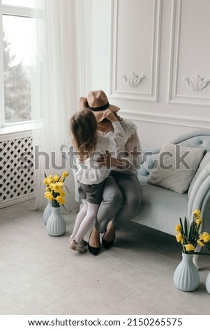 Smiling young mother and little daughter cuddle have fun sitting on couch at home, overjoyed mom or nanny playing with small preschooler girl child tickle and laugh, enjoy leisure weekend at home