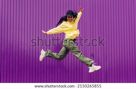 Jumping young woman in yellow dress on purple background. Dancer of hip hop and trap music. Concept of freedom, celebration, joy. Royalty-Free Stock Photo #2150265855