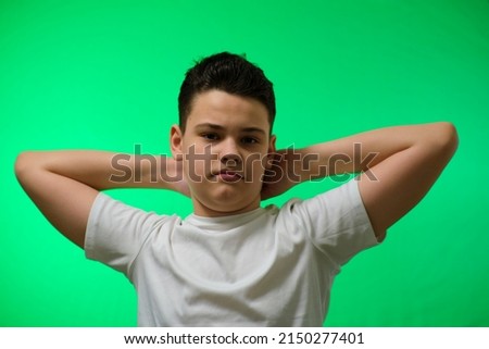 a boy on a green background looks at the camera,hands up, not smiling,angry,resting,portrait