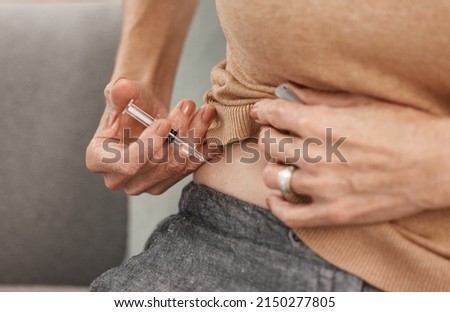 Managing diabetes one shot at a time. Shot of a mature woman injecting herself with insulin on the sofa at home. Royalty-Free Stock Photo #2150277805