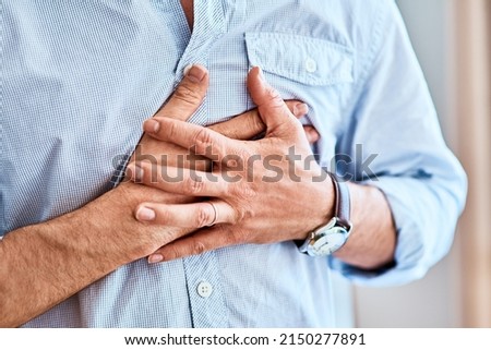 Chest pains are never a good sign. Shot of a unrecognizable man holding his chest in discomfort due to pain at home during the day. Royalty-Free Stock Photo #2150277891