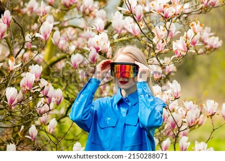 Stylish woman in glasses and blue shirt and VR glasses near Magnolia tree in spring time