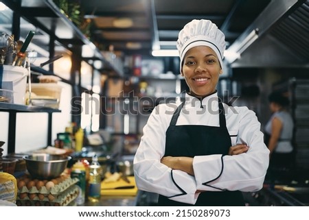 Happy African American woman standing with arms crossed while working as chef in a restaurant and looking at camera. Royalty-Free Stock Photo #2150289073
