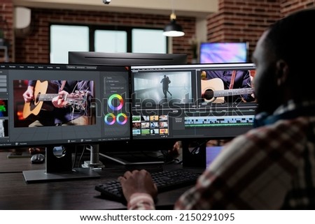 Professional post production editor doing footage montage and visual improvement. Creative agency office employee sitting at multi monitor workstation while editing graphic content on computer.